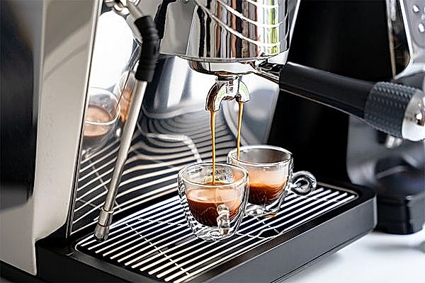 2 Espressotassen stehen in einer Kaffeemaschine und werden von ihr befüllt