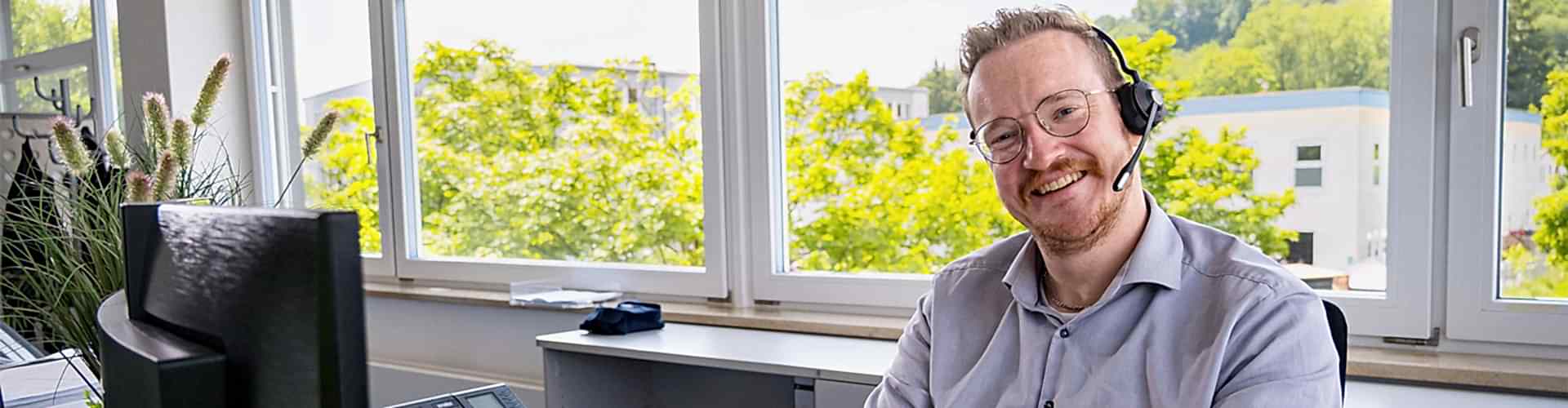 Mitarbeiter sitzt vor seinem Monitor am Schreibtisch und lächelt